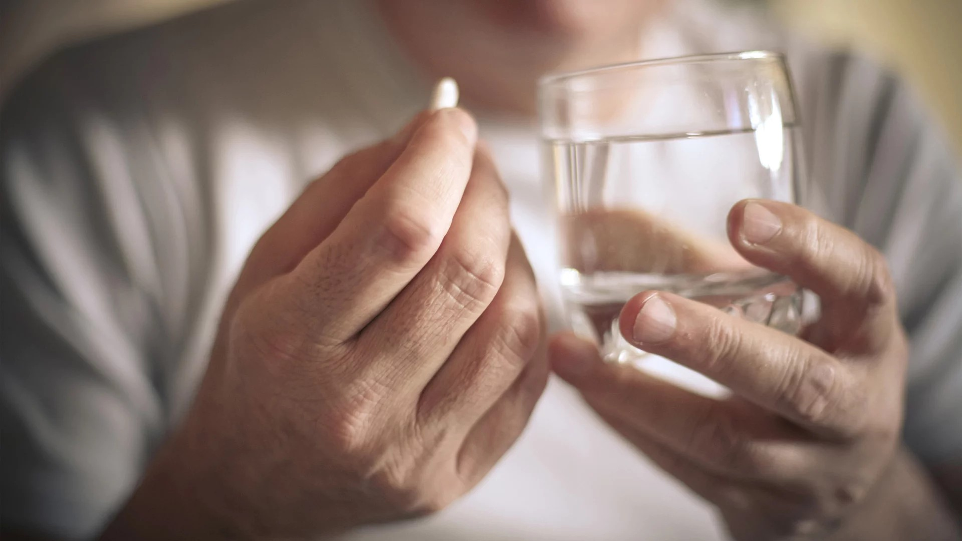 Person hält in einer Hand Wasserglas in der anderen eine Tablette.