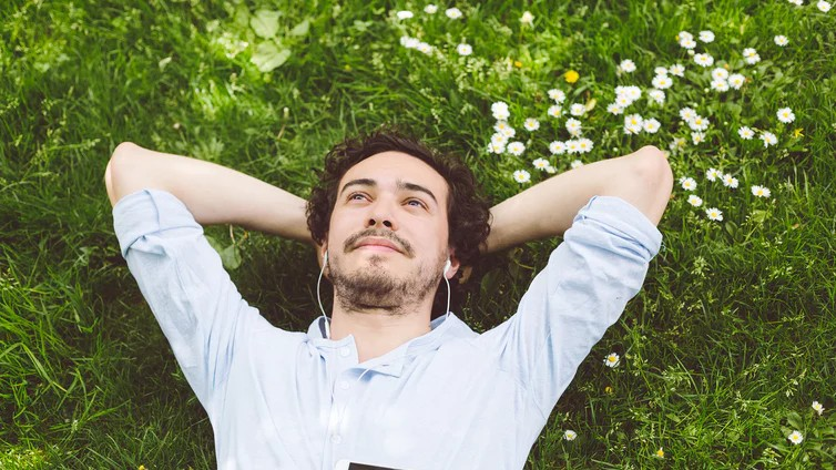 Mann liegt auf einer Wiese. Arme hinter dem Kopf verschränkt.