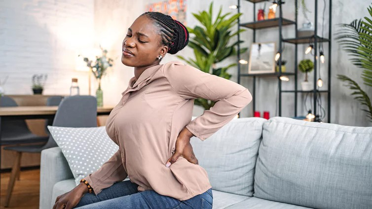 Frau auf Sofa fasst sich an den Rücken.