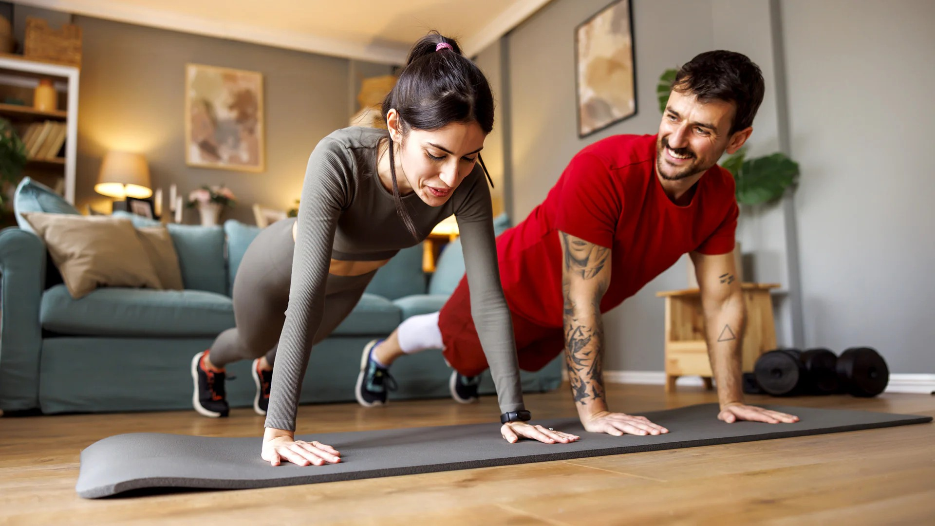 Fotografie eines gemeinsamen Heimtrainings mit zwei Personen bei Liegestützen auf einer Matte im Wohnzimmer.