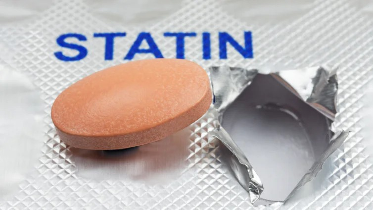 Fotografie einer orangefarbenen Statin-Tablette neben einer geöffneten Blisterpackung. Blaue Aufschrift „STATIN“ kennzeichnet das Medikament zur Senkung erhöhter Cholesterinwerte.
