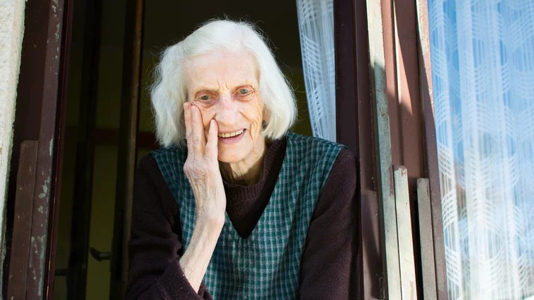 Alte Frau mit weißen Haaren schaut aus dem offenen Fenster
